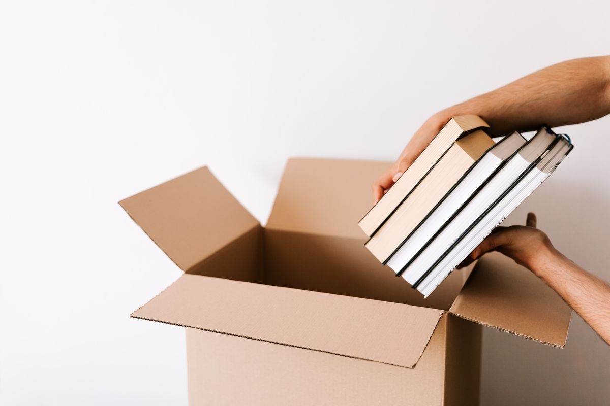 A box of used books being packed by hand